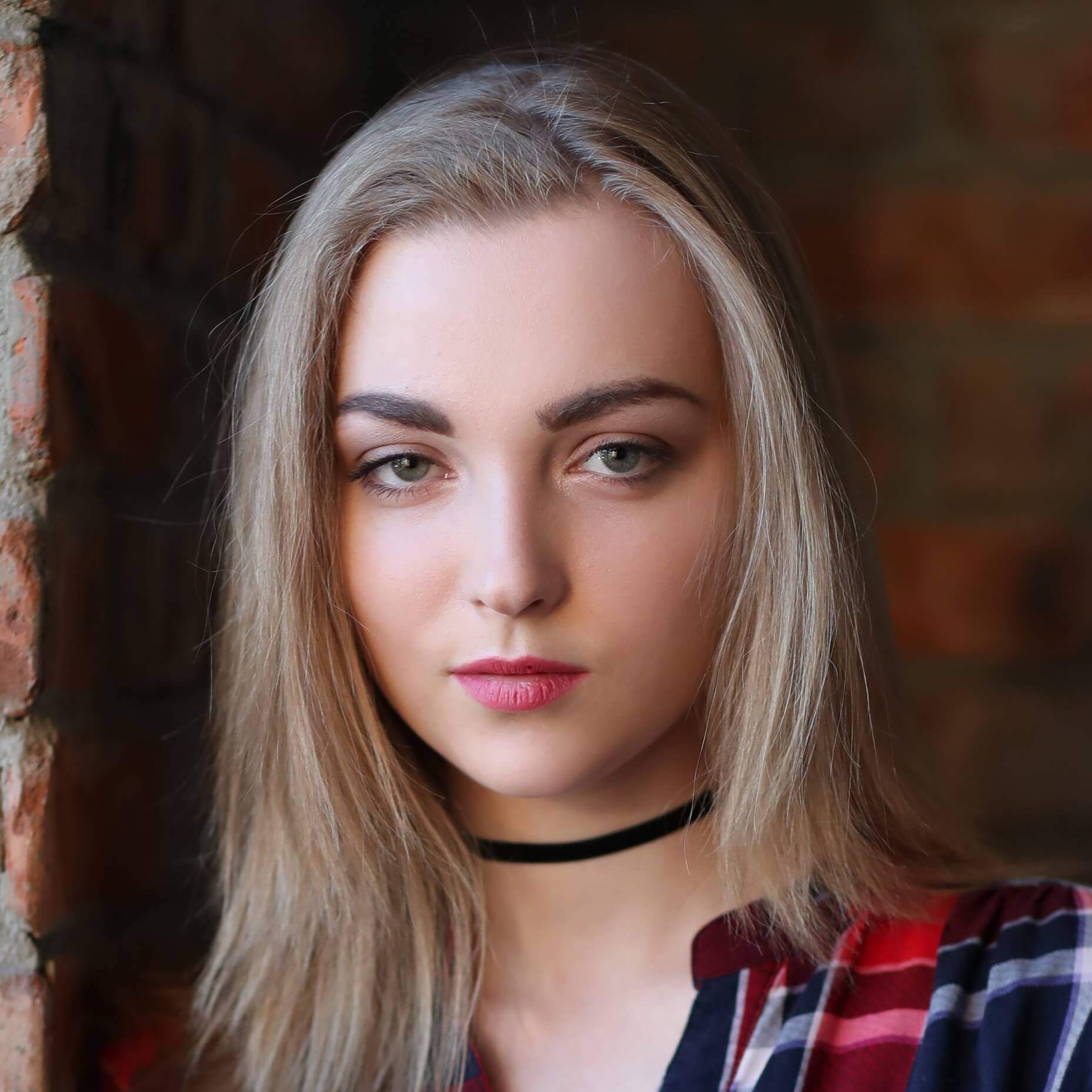Femme blonde posant devant un mur de briques.